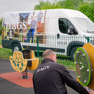 HAGS employee checks playground installation, with a HAGS van in the background.